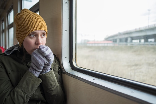 Sad woman rides on the train. she is cold and warms her gloved\
hands with her breath