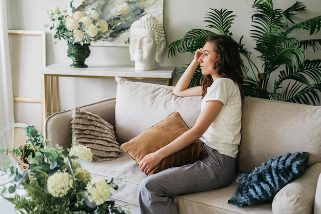 Photo a sad woman sits on a sofa at home hugging a pillow