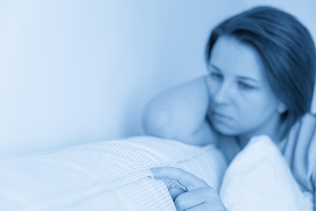 Грустная женщина сидит на кровати и держит подушку