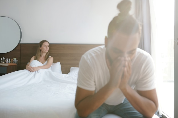 Sad woman sitting in bed and looking at window after having bad\
sex with boyfriend