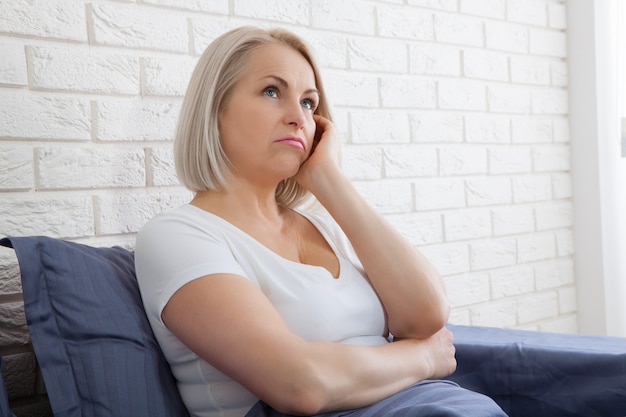 Sad woman sitting on the bed at the morning. Depressed menopause. 