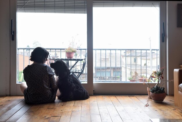 Sad woman sitting and looking out the window with her dog