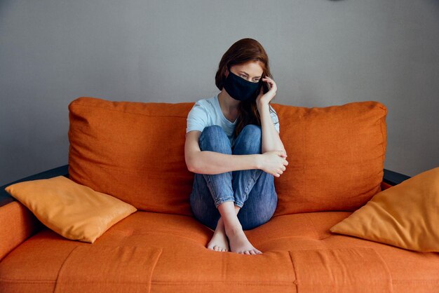 Sad woman sitting on the orange sofa at home in protective masks Lifestyle