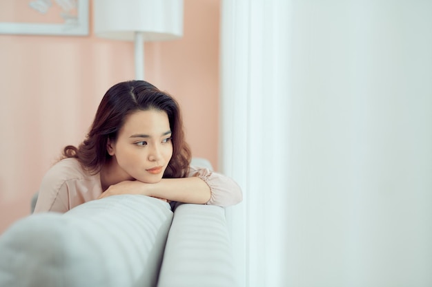 Sad woman sitting on sofa at home deep in thoughts, thinking about important things