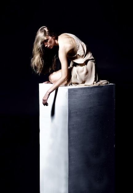 Sad woman sitting on a stone pedestal studio shot dark background