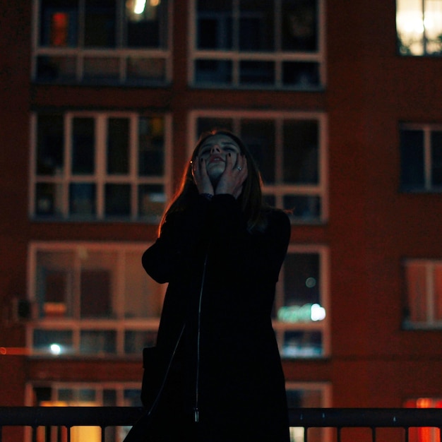 Фото Печальная женщина, стоящая против здания ночью.