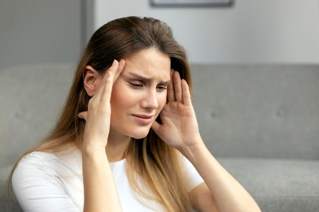 Sad woman suffering from headache or migraine, feeling sick, sitting at home. Depression concept