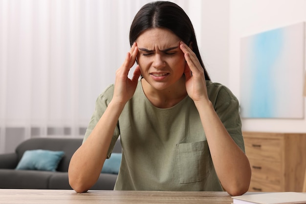 sad woman suffering from headache at wooden table indoors