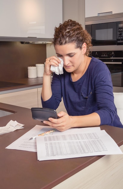 Photo sad woman using calculator by papers on table at home