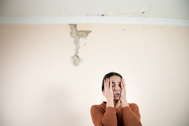 Photo sad woman with damaged ceiling and wall