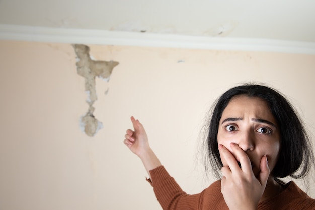 Sad woman with damaged ceiling and wall