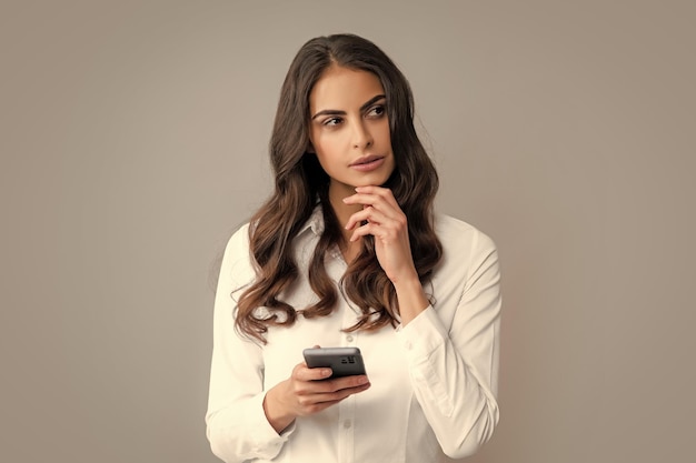 Sad woman with smart phone Young woman with mobile phone Serious business woman with smartphone on grey background