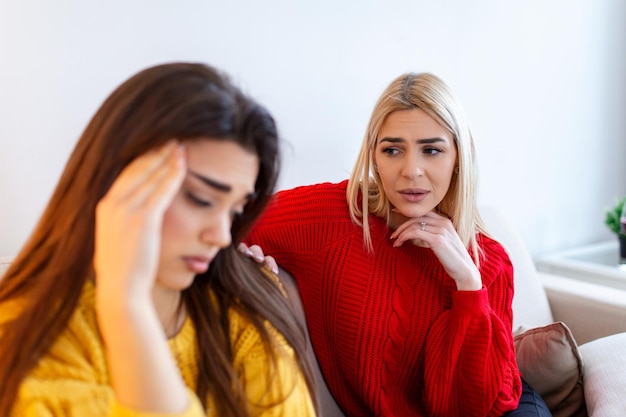 Sad women and supporting friends trying to solve a problem two\
sad diverse women talking at home female friends supporting each\
other problems friendship and care concept