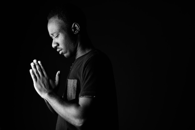 Sad young African man praying in black and white