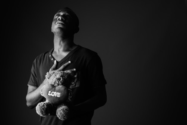 Sad young African man with teddy bear and love sign text thinking