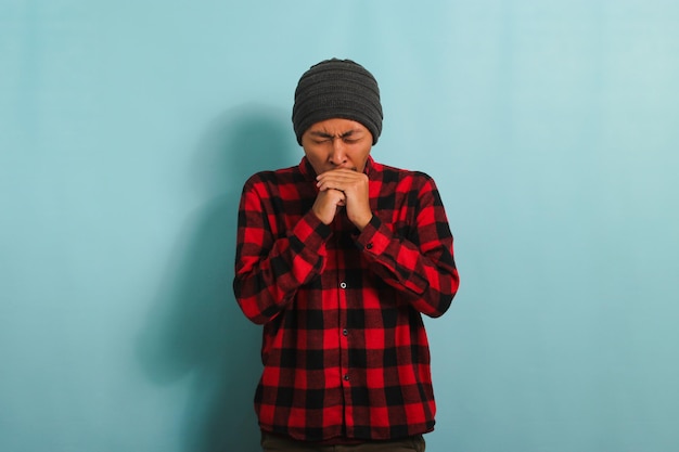 A sad young Asian man is suffering from fever and flu isolated on a blue background