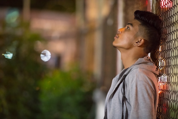 Sad young Asian man leaning on fence in the city street at night