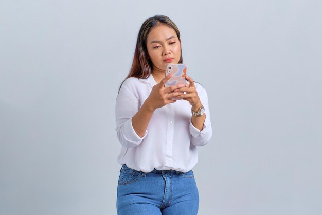 Sad young Asian woman looking at mobile phone screen reacting to bad news isolated over white background