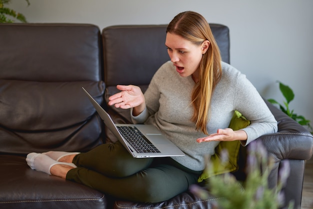 ソファでラップトップコンピューターを使用して悲しい若い美しい女性