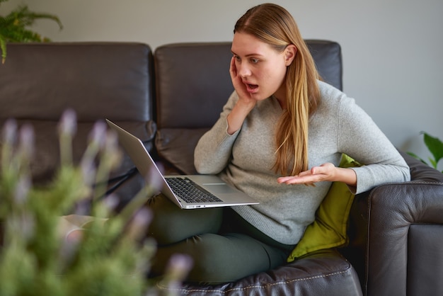 ソファでラップトップコンピューターを使用して悲しい若い美しい女性