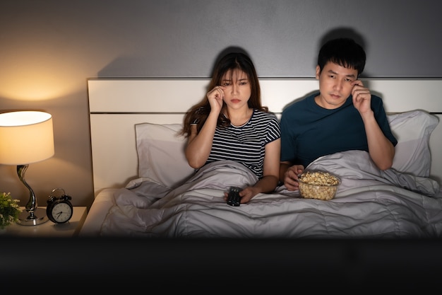 Triste giovane coppia guardando la televisione e piangendo su un letto di notte (film romantico)