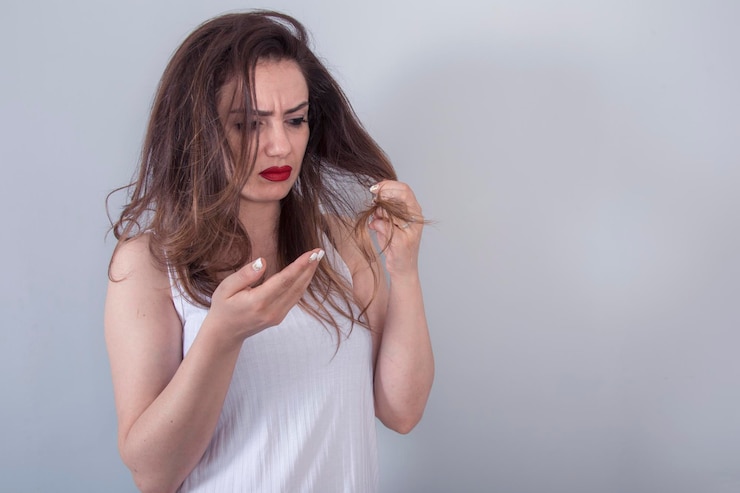 Sad young cute girl looks at her damaged hair with shock