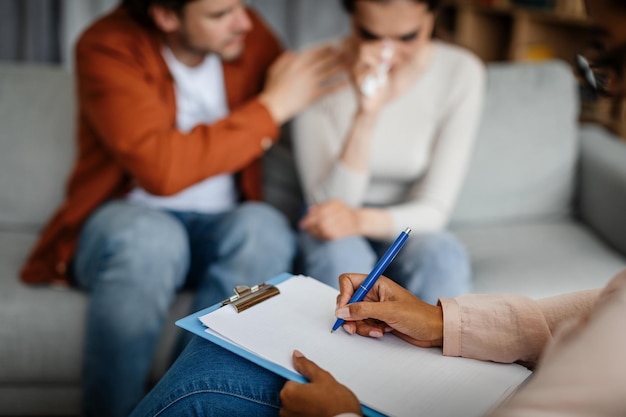 Sad young european guy calms crying wife at meeting with psychologist in office clinic interior close up