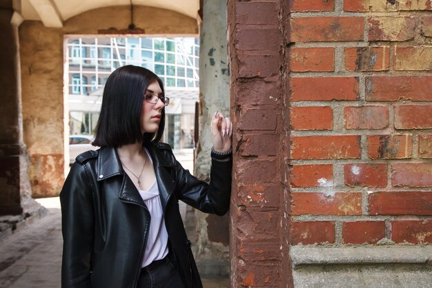 Photo sad young girl in black jacket and jeans stands in old arch on city street on summer day