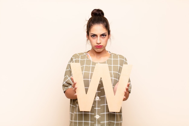 Photo sad young girl holding the letter w of the alphabet to form a word or a sentence