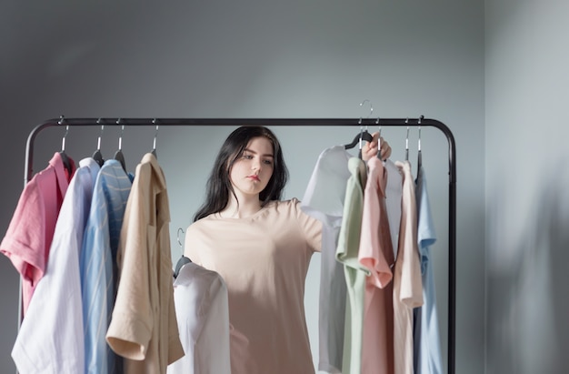 Sad young girl next to summer clothes on  hanger at home