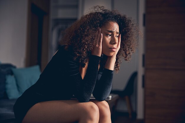 Sad young lady in a stylish evening dress sitting alone on the sofa