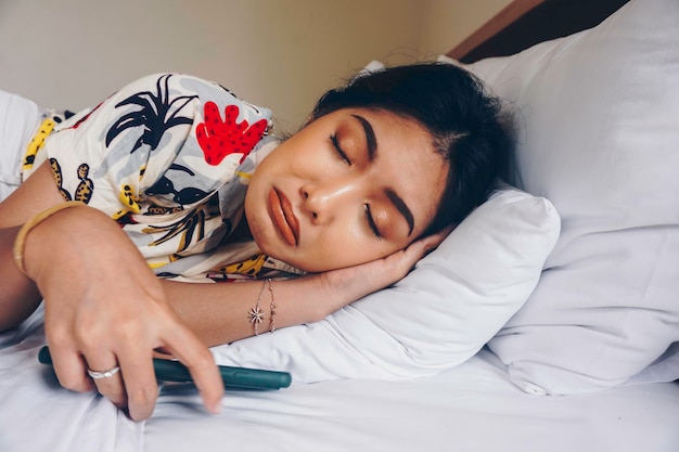 Sad young woman frowning from the bed waiting for a call while holding the smartphone