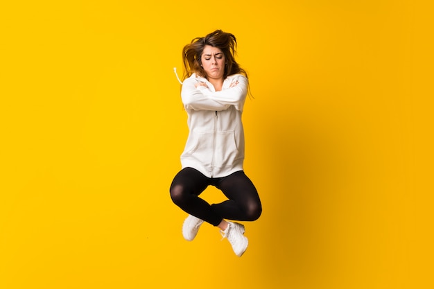 Sad young woman jumping over isolated yellow wall