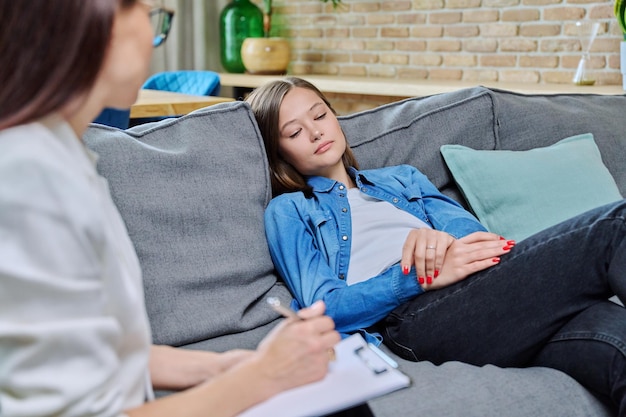 Sad young woman in meeting with psychologist sitting on couch in office