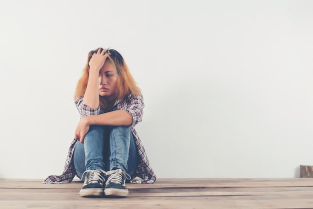 sad young woman sitting against white wall