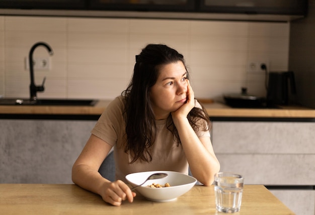 sad young woman sitting in the kitchen having breakfast a plate of oatmeal and a glass of water on the table