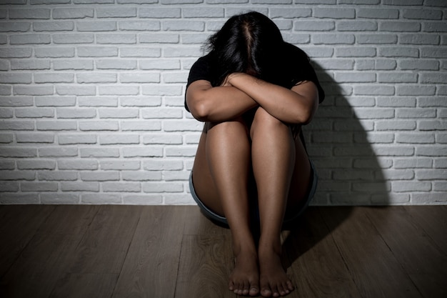 Sad young woman sitting near the wall.