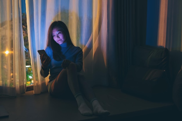 A sad young woman using mobile phone with bright light screen in the late night at home