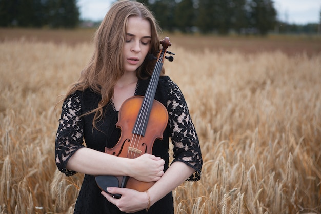 落ち込んだ目を持つ悲しい若い女性バイオリニストは、彼女にバイオリンを優しく押します
