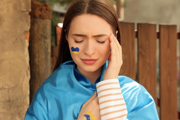 Грустная молодая женщина с рисунком украинского флага на лице на улице