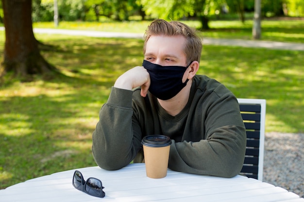 Sadness Man in a protective black mask sitting at a table in a cafe