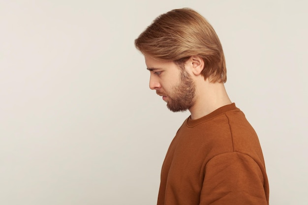 Sadness and resentment emotions. Profile of unhappy bearded man in sweatshirt looking down, bowing head