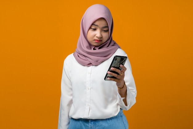 Женщина грусти молодая азиатская используя мобильный телефон на желтом
