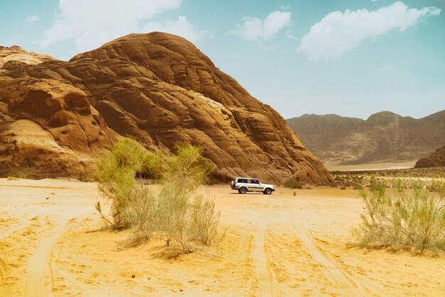 Photo safari jeep car in wadi rum desert jordan middle east known as the valley of the moon sands blue sky clouds designation as a unesco world heritage site