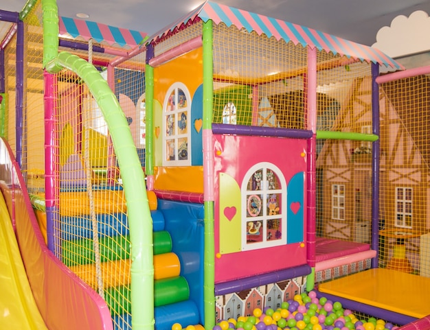 실내 놀이터에 있는 집 형태의 그물과 다채로운 공이 있는 안전한 다채로운 어린이 트램폴린.