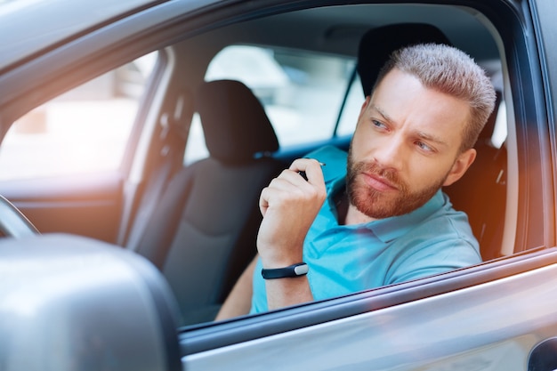 Safe driver. Beautiful bearded young man sitting in his car, holding keys