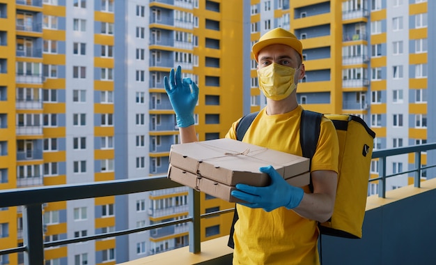 Safe food delivery. Courier in yellow uniform, protective mask and gloves delivers takeaway food during coronovirus quarantine