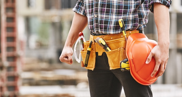 Фото Обрезанное фото мужчины-строителя со строительными инструментами, держащего безопасный красный цвет, безопасная работа