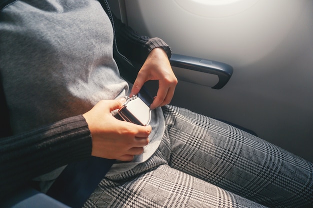 Safety concept Asian Woman is Fastening Seat belt on Airplane Ready to Take off