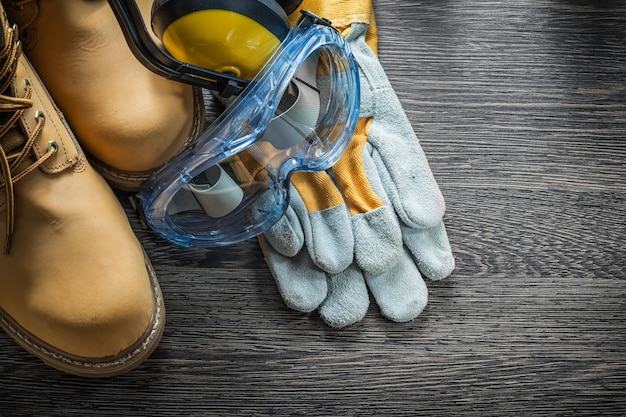 Safety gloves boots glasses ear muffs on wooden board.